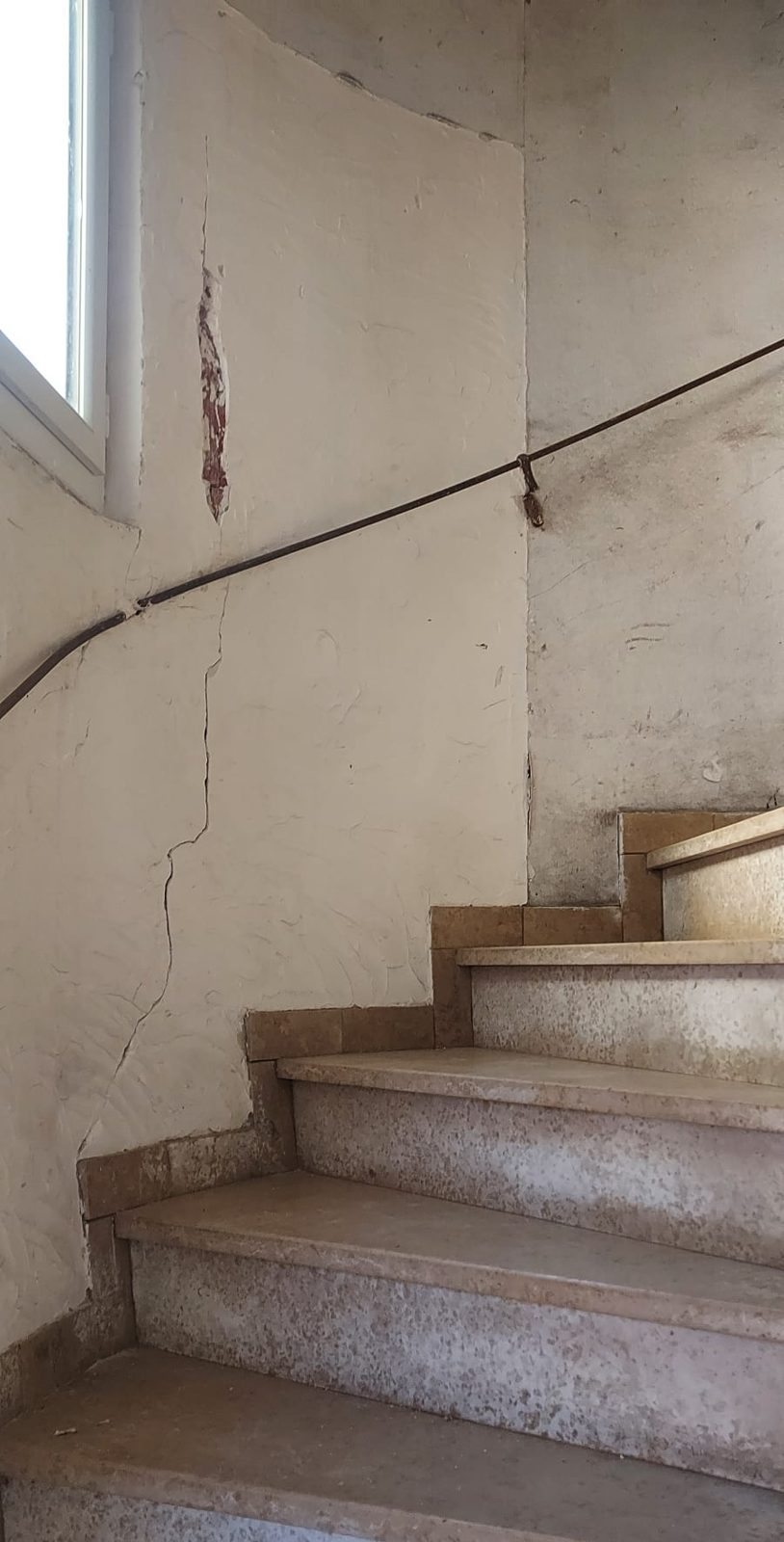 Avant travaux : escalier tournant aux murs fissurés et écaillés
